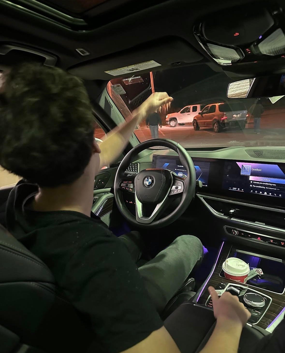 Person sitting in drivers seat of a modern BMW car with illuminated dashboard and infotainment screen